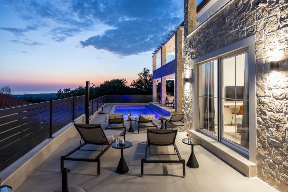 Moderne Terrasse mit Pool, Liegen und Aussicht auf das Meer bei Sonnenuntergang.