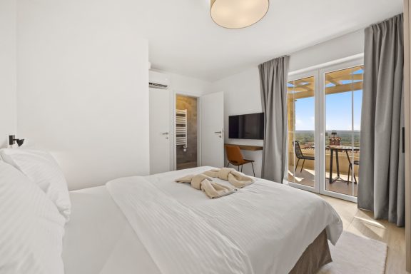 Helles Schlafzimmer mit Doppelbett, Balkon und Blick auf die Landschaft.