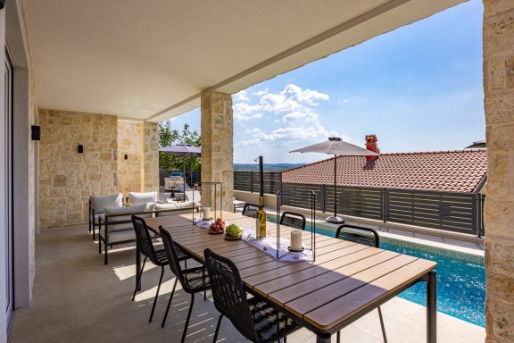 Moderne Terrasse mit Esstisch, Pool und Blick auf ruhige Landschaft.